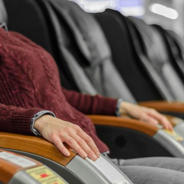 titan ti-7700 massage chair features zero gravity woman in burgundy sweater sits in massage chair getting a massage black massage chairs in a row in the background